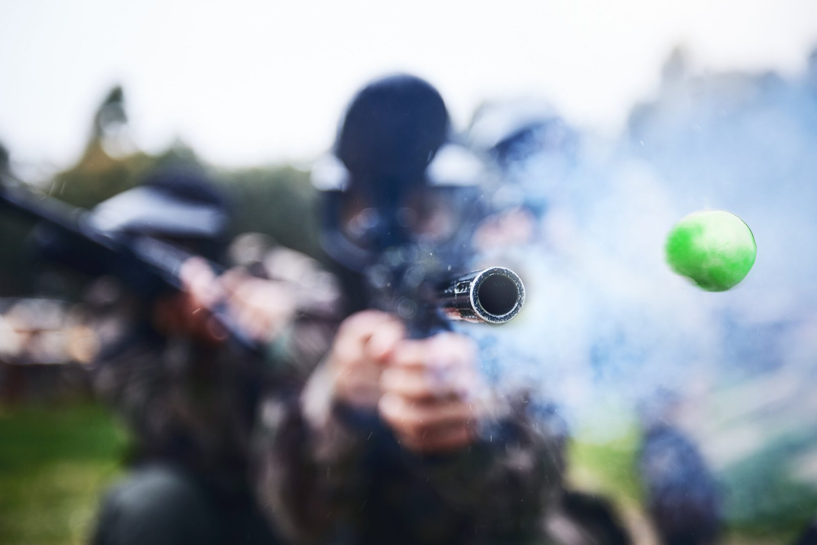 Paintball, shooting and person with a gun during a game, competition or match on a field. Fire, smoke and tool in motion for attack, battle and aim with a weapon during an outdoor cardio sport.